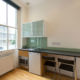Kitchenette with a microwave, fridge, hob and two chars in a studio apartment